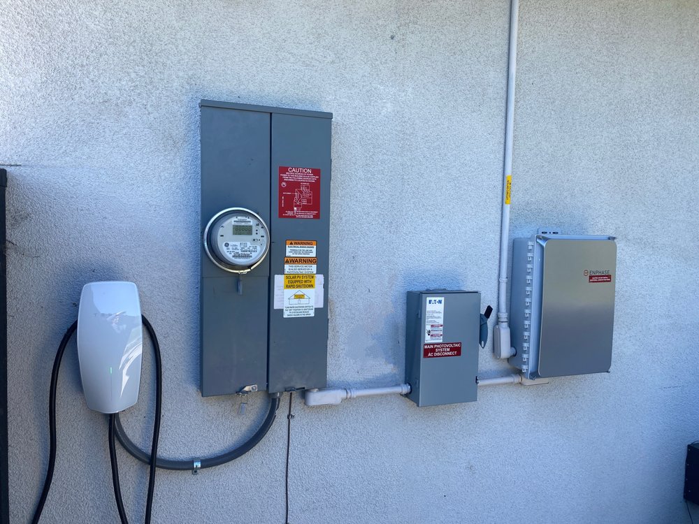 Utility meter, main PV disconnect, and Enphase combiner box mounted on the exterior wall with EV charger