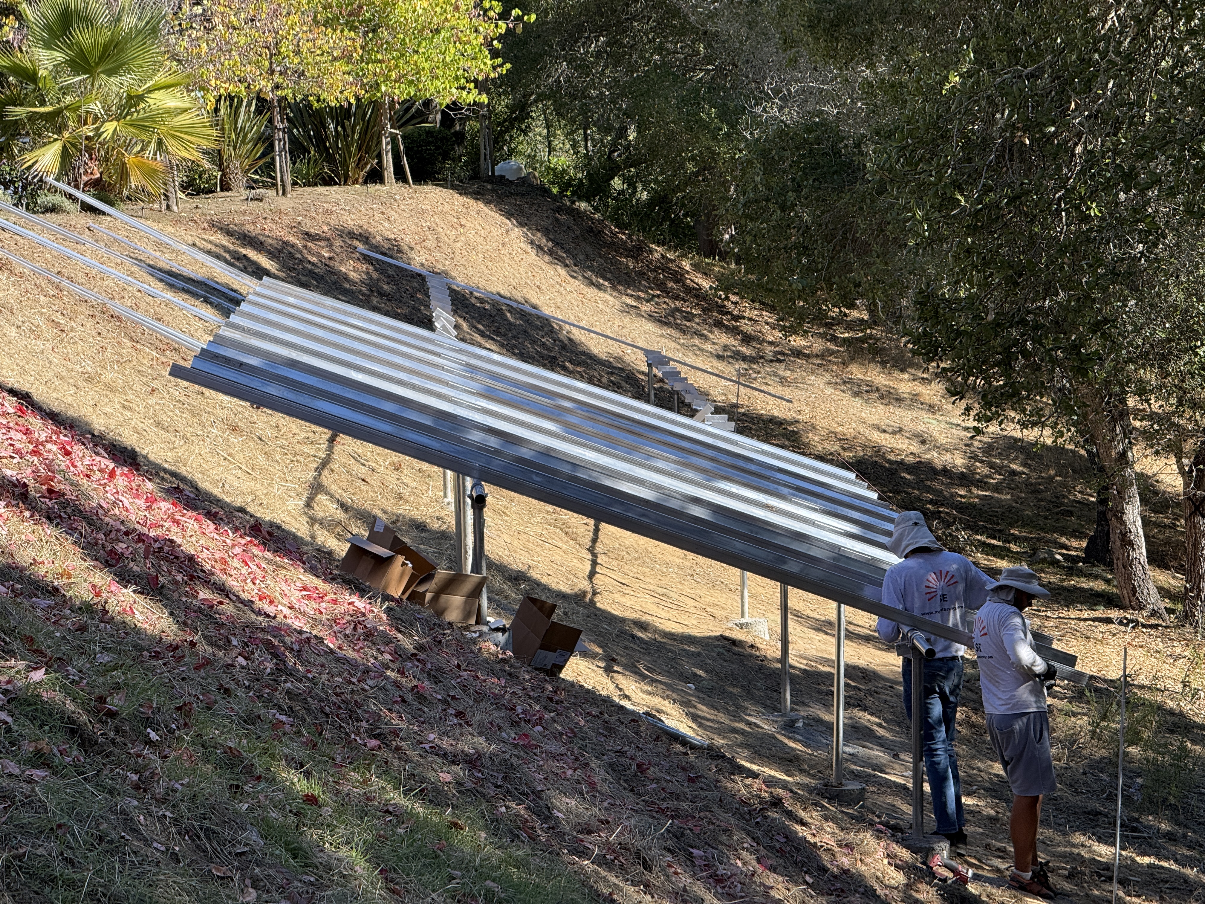 Crew installing ground-mount solar racking on a wooded hillside lot