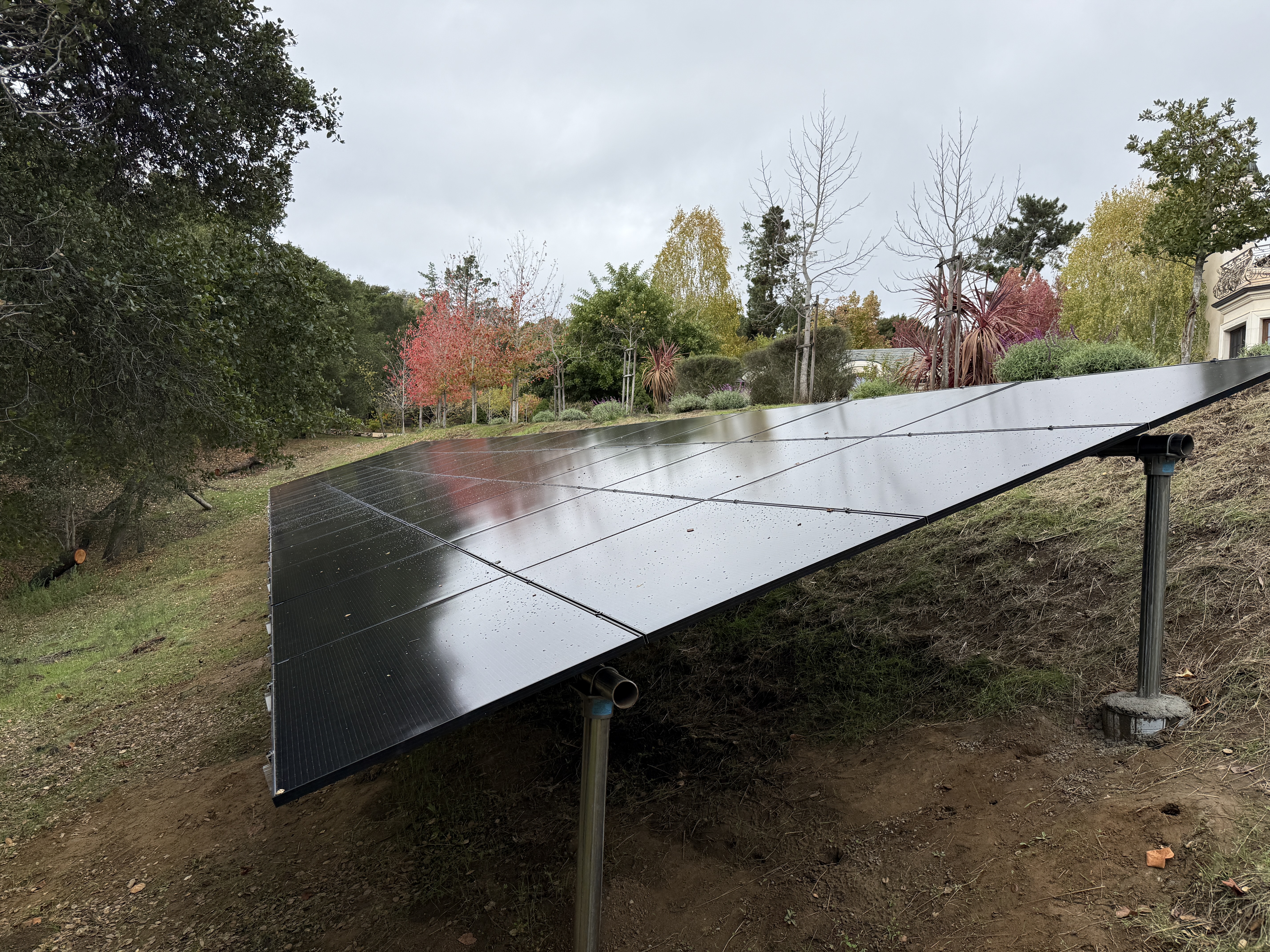 Completed ground-mount solar array of black panels on a hillside