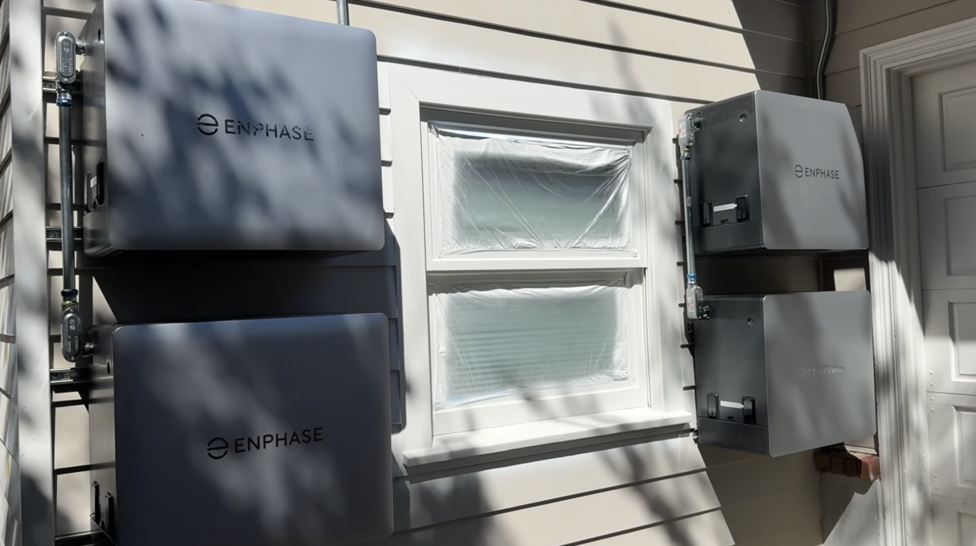 Four Enphase IQ Battery 10C units mounted on the exterior wall around a window